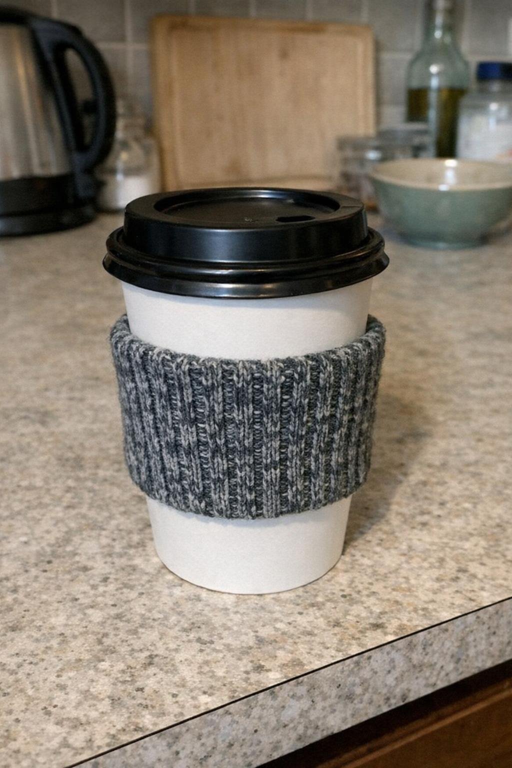 A takeaway coffee cup covered with a ribbed sock cuff sleeve