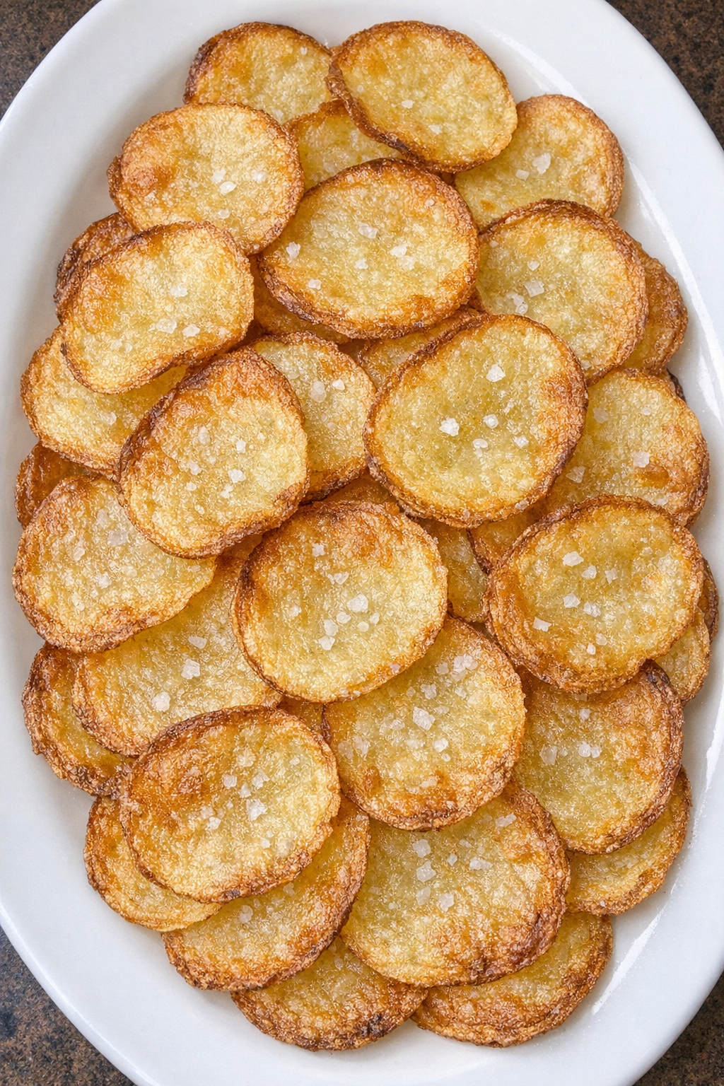 Paper-thin crispy golden potato wafers on a white oval platter