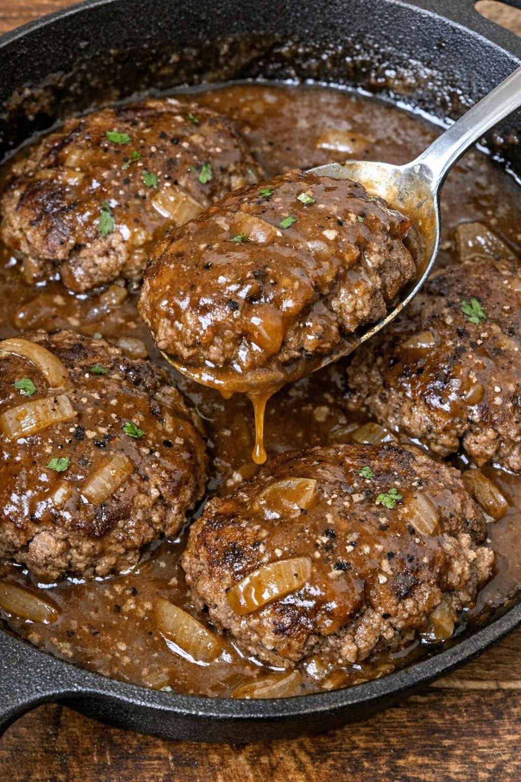 Hamburger steaks in brown gravy in a cast iron skillet