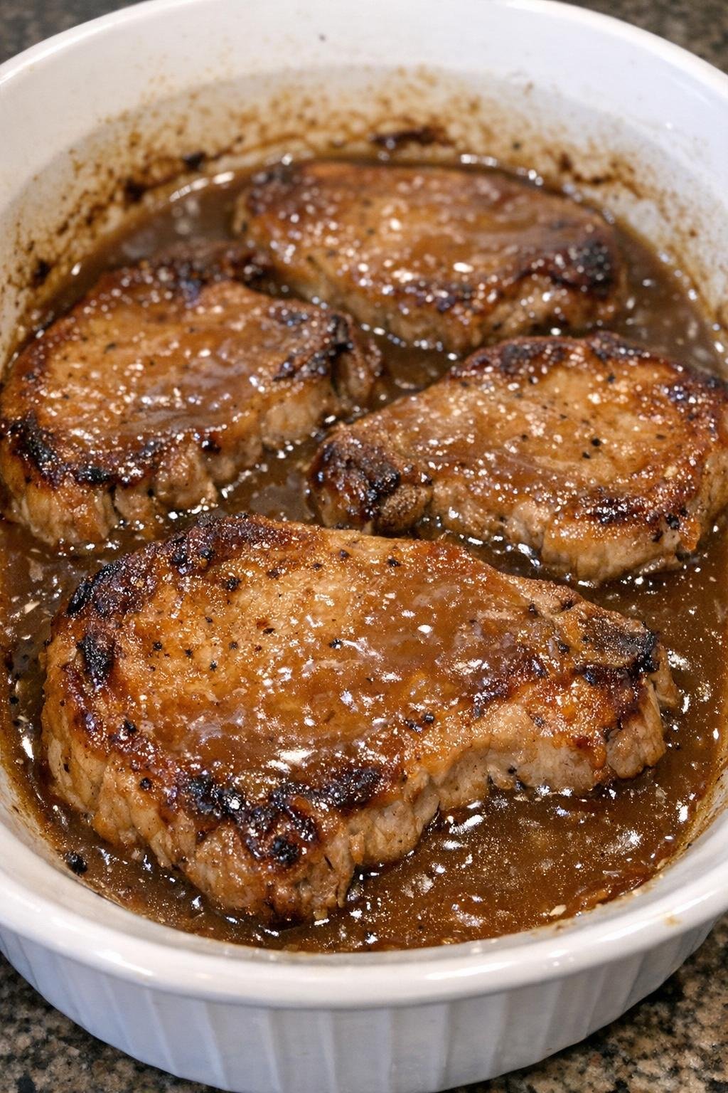 Tender pork chops in brown gravy baked in a white casserole dish