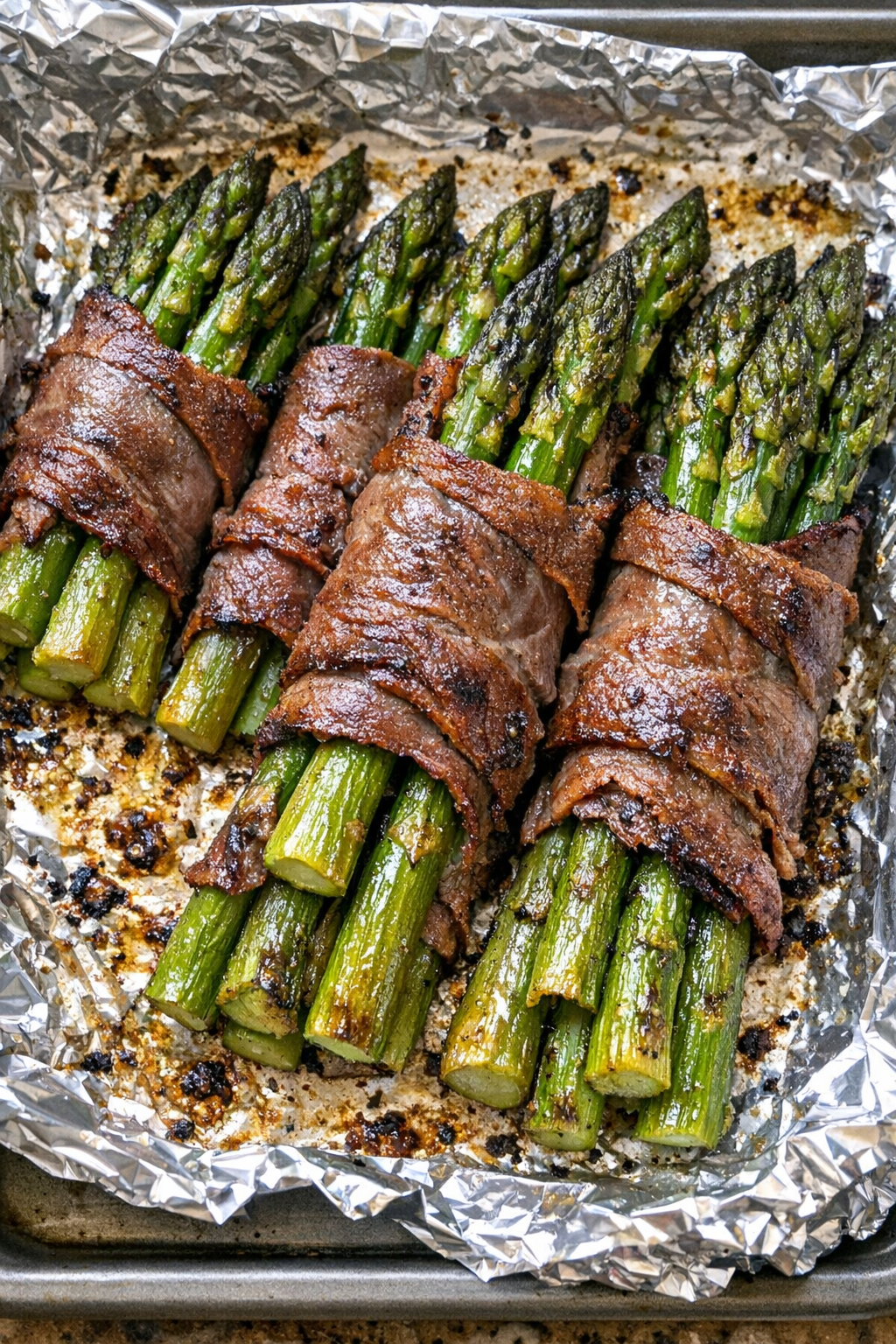 Oven baked beef wrapped asparagus on a foil-lined baking sheet