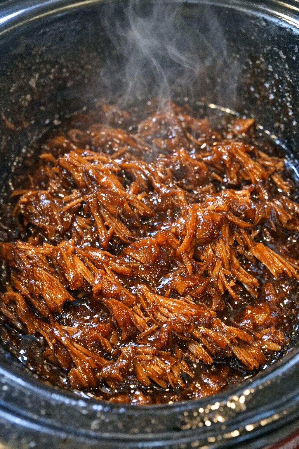 Succulent pulled protein glazed in dark amber sauce in a slow cooker