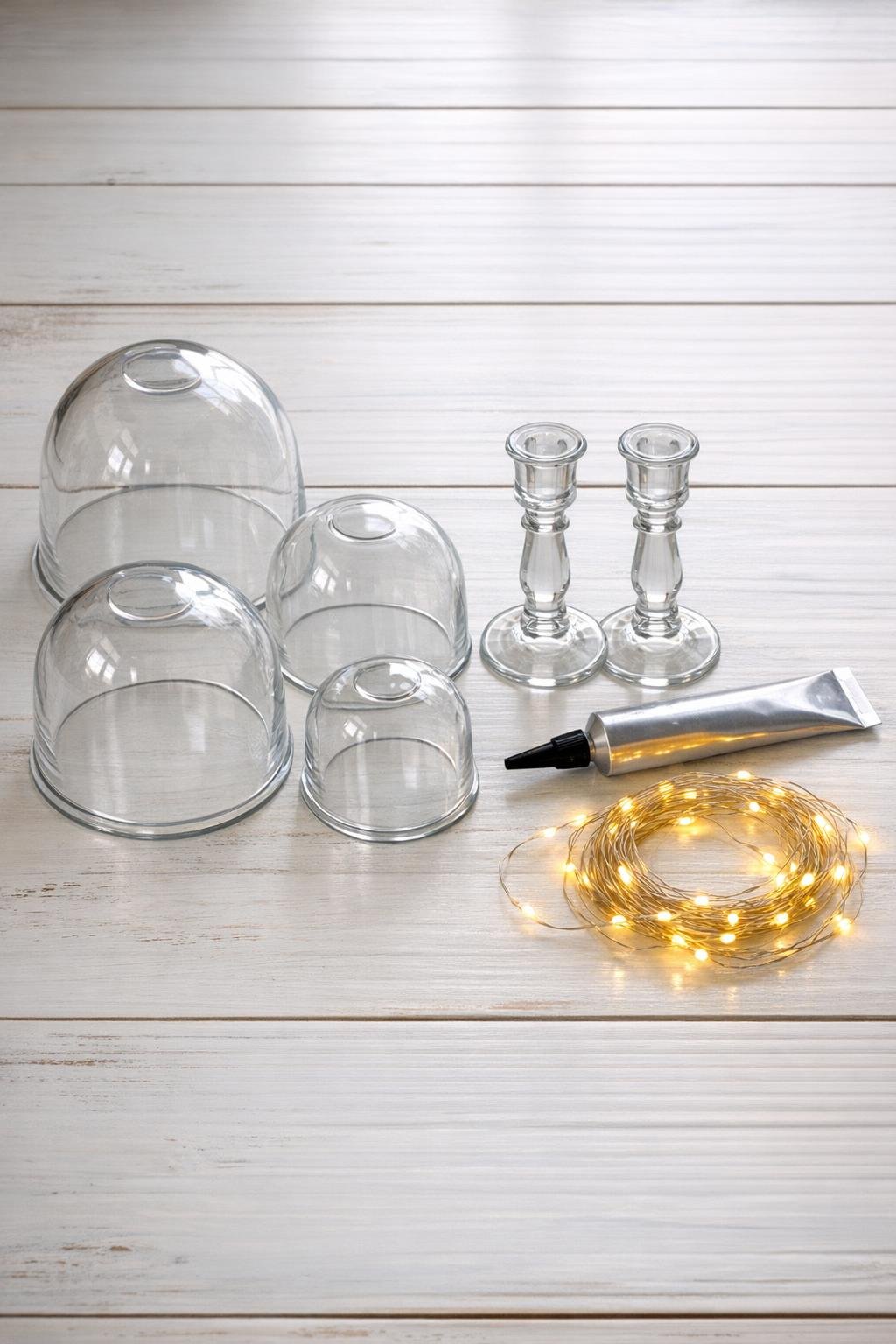 Glass light covers, candlesticks, adhesive, and fairy garland laid out for the project