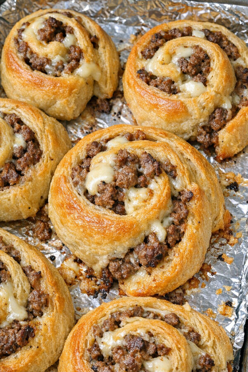 Oven baked beef crescent swirls on a foil-lined baking sheet