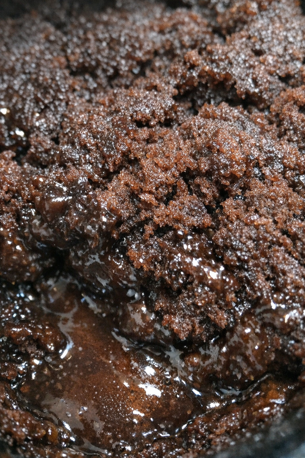 Close-up of a glistening cocoa-colored dessert with sticky sauce and craggy texture