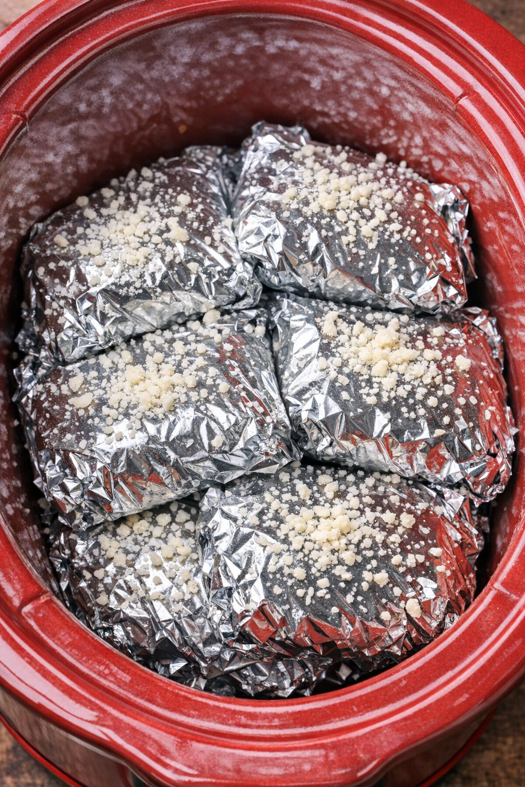 Foil-wrapped cheesy marinara rotini packets in a red slow cooker