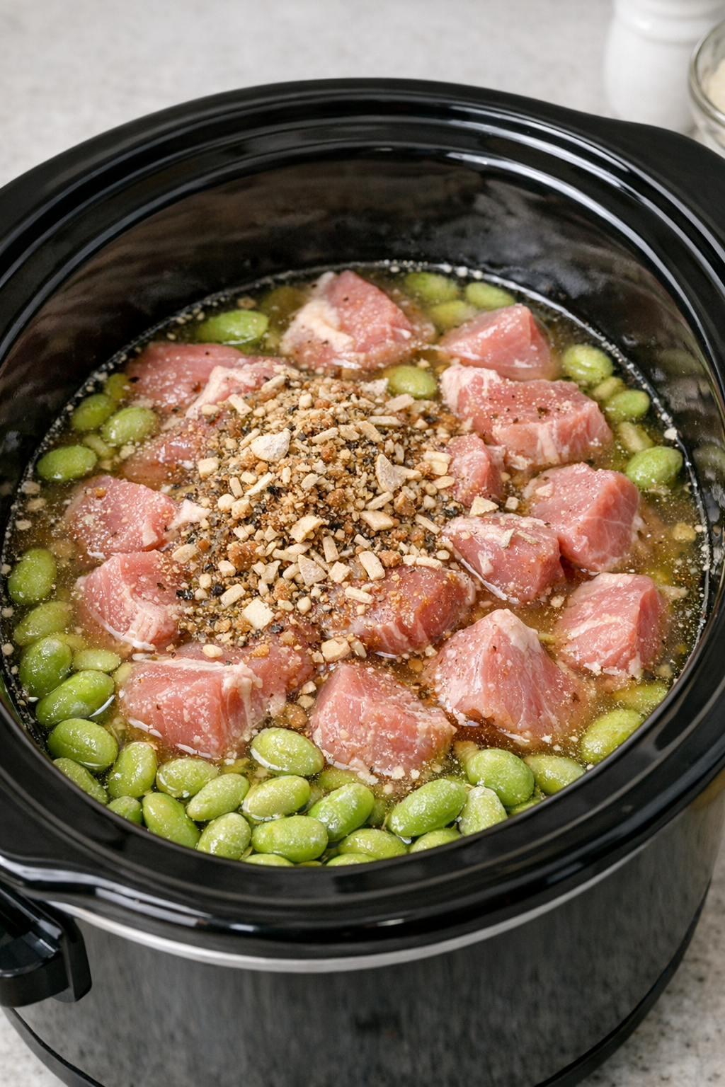 Slow cooker filled with broth, pork, beans, and seasoning before cooking