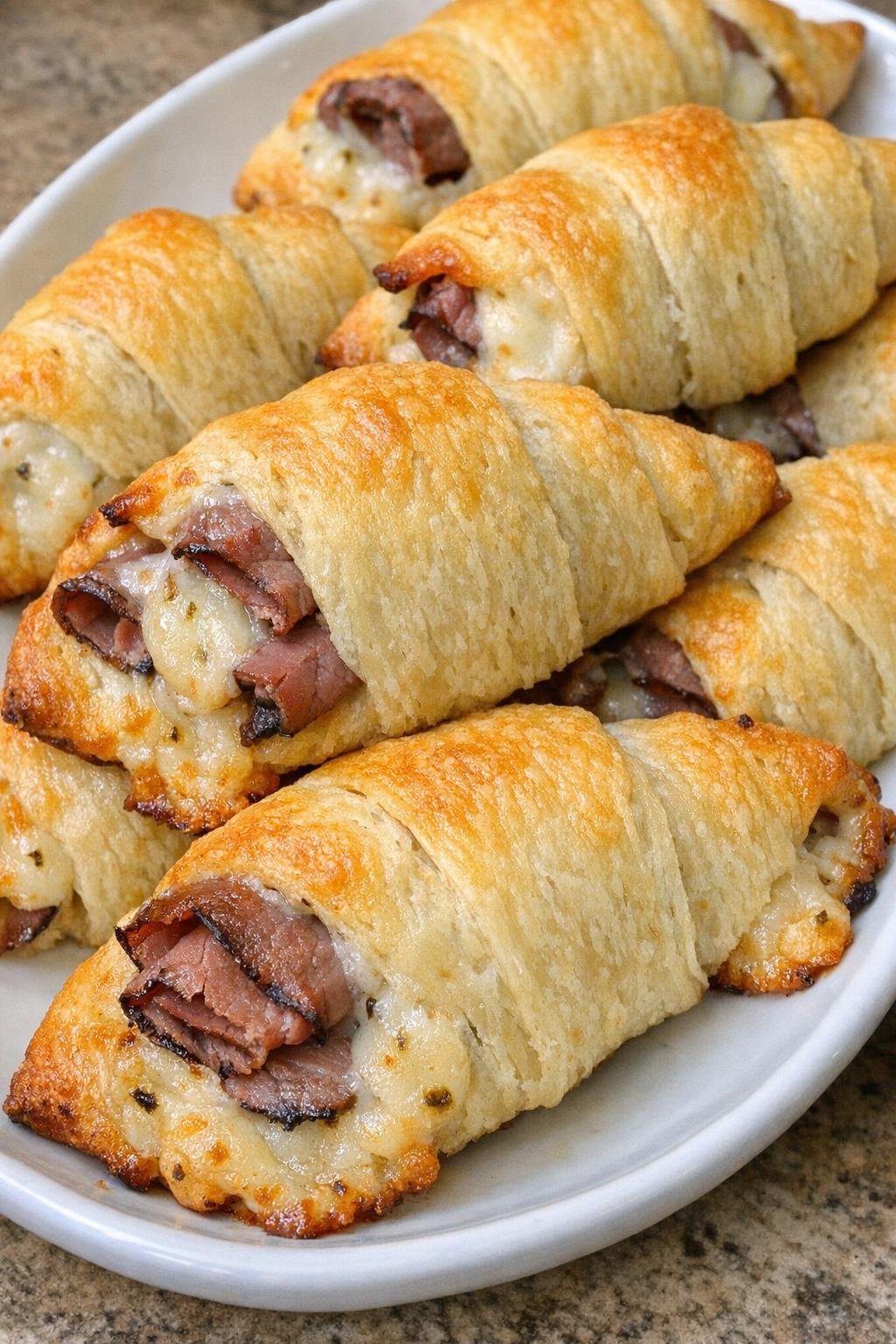 Golden brown crescent horns filled with roast beef and pepper jack cheese on a white platter