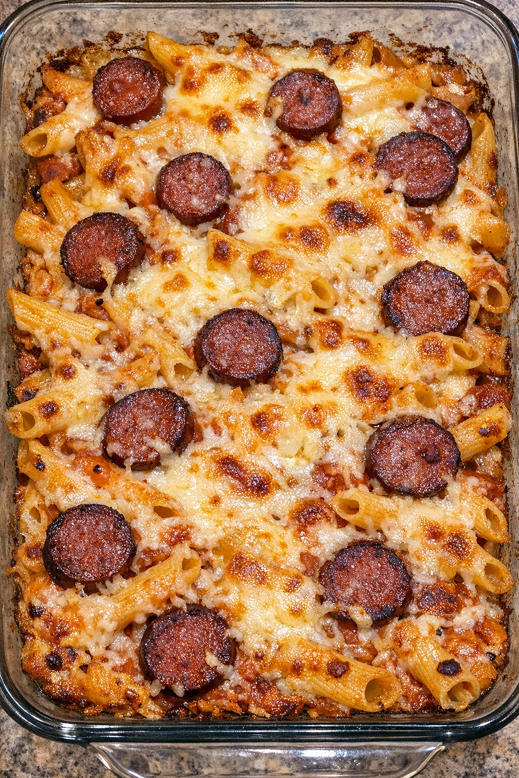 Baked ziti with summer sausage and white cheddar in a glass dish