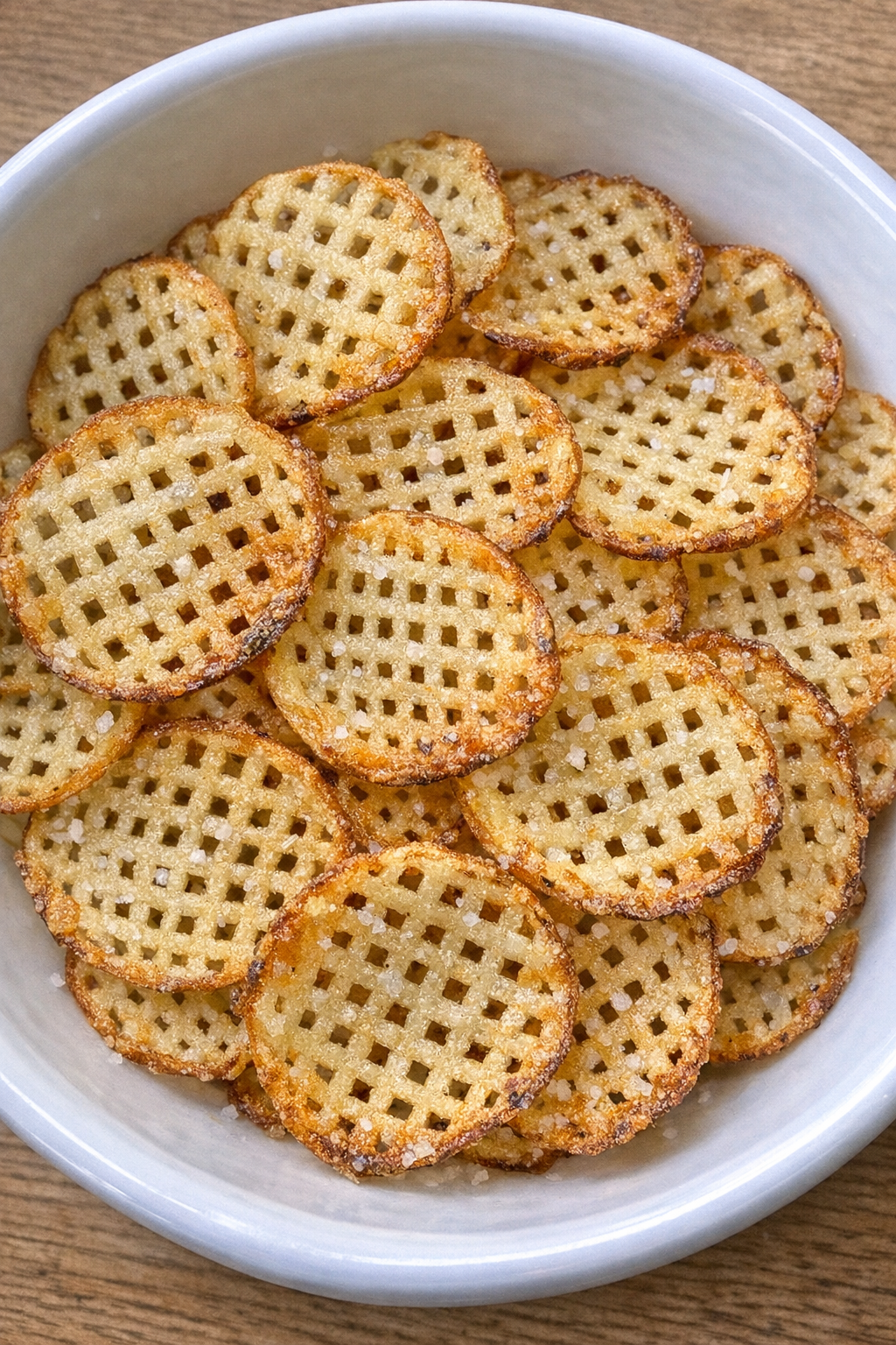 Golden crispy lattice-cut potato chips in a white ceramic bowl