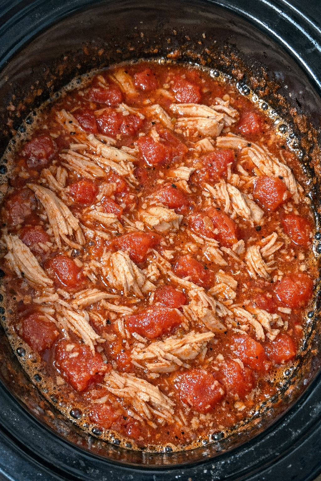 Slow cooker stewed tomato chicken in a black slow cooker