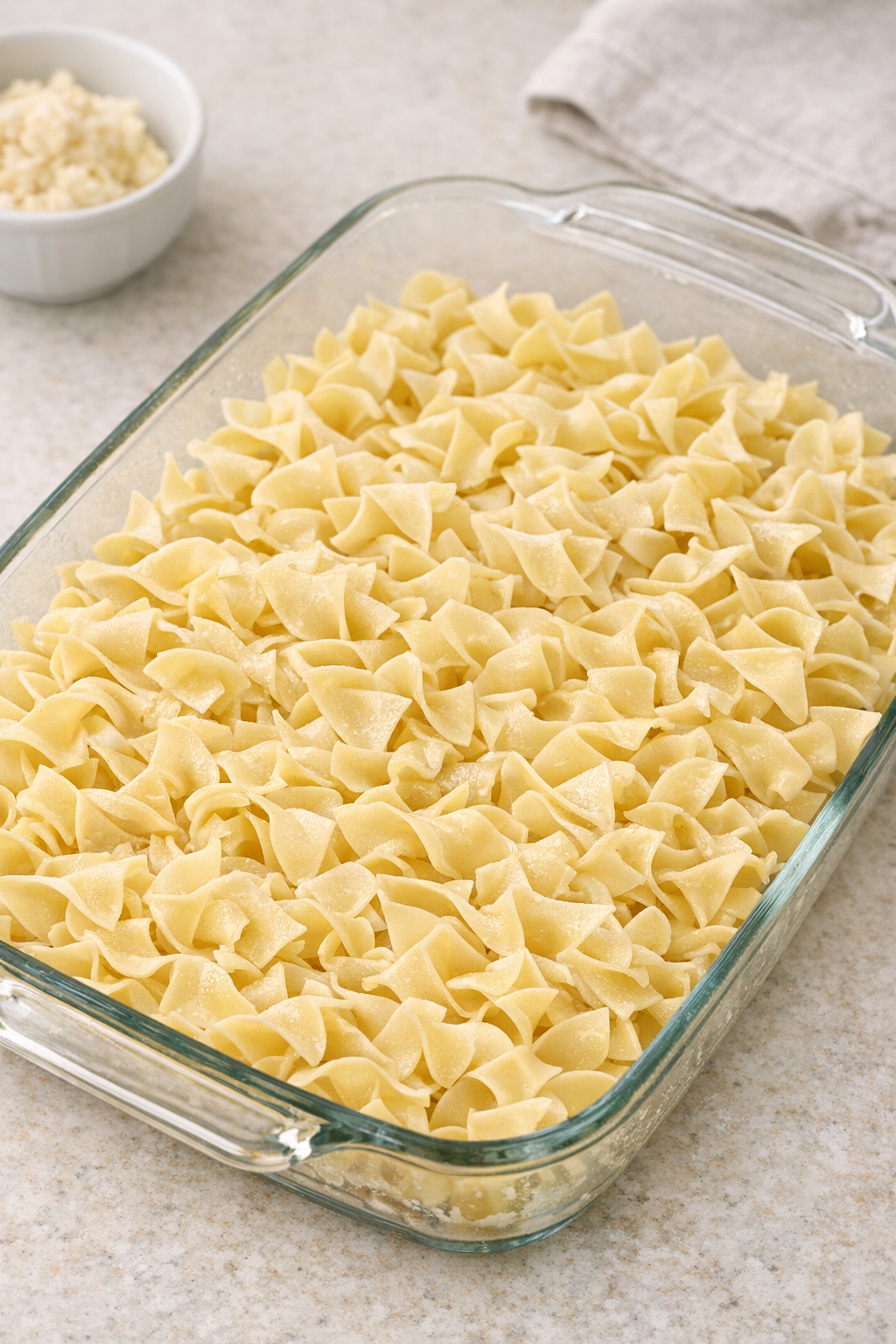 Uncooked wide egg noodles spread in a casserole dish
