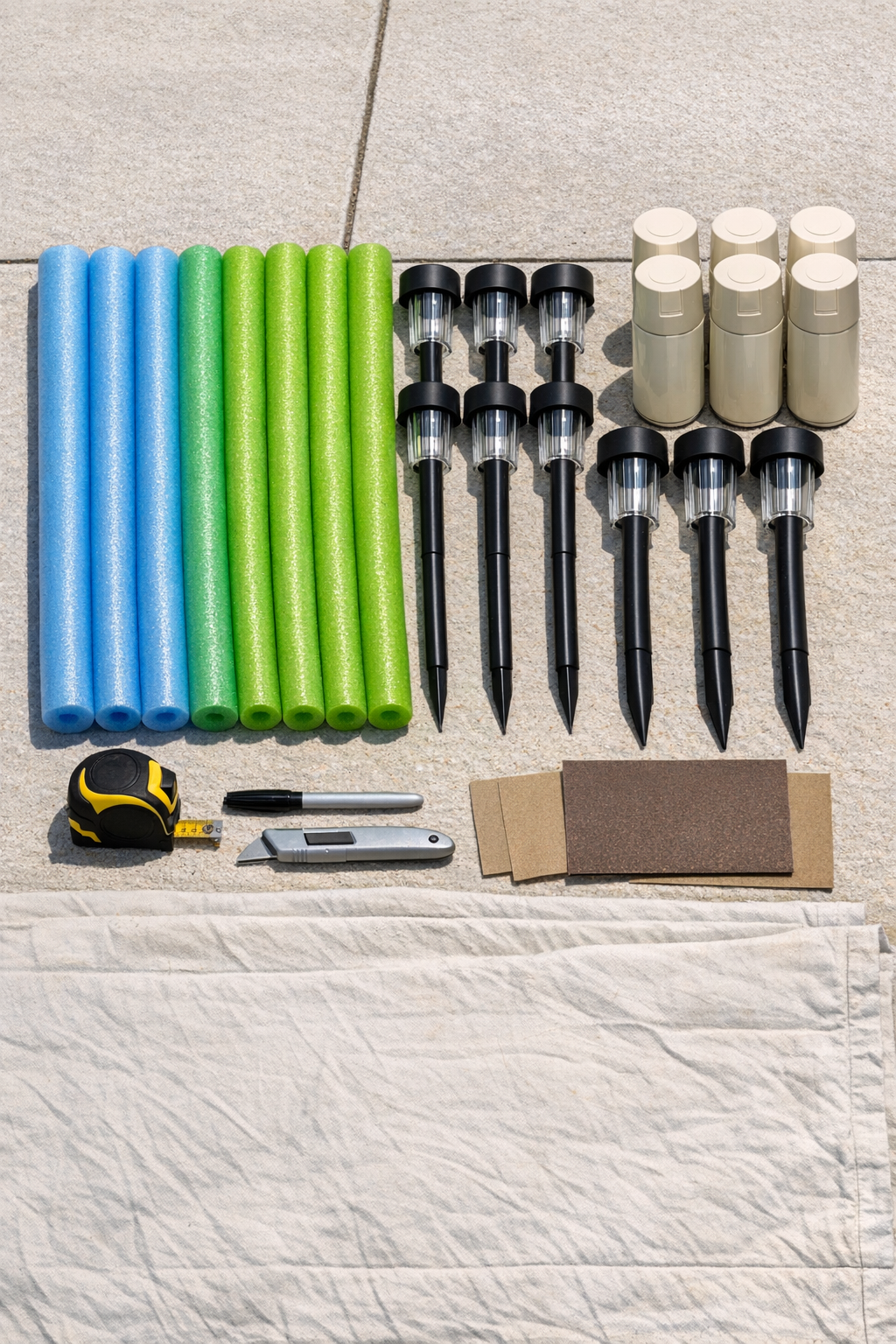 Pool noodles, matte ivory spray paint, and tall solar path lights laid out for the project
