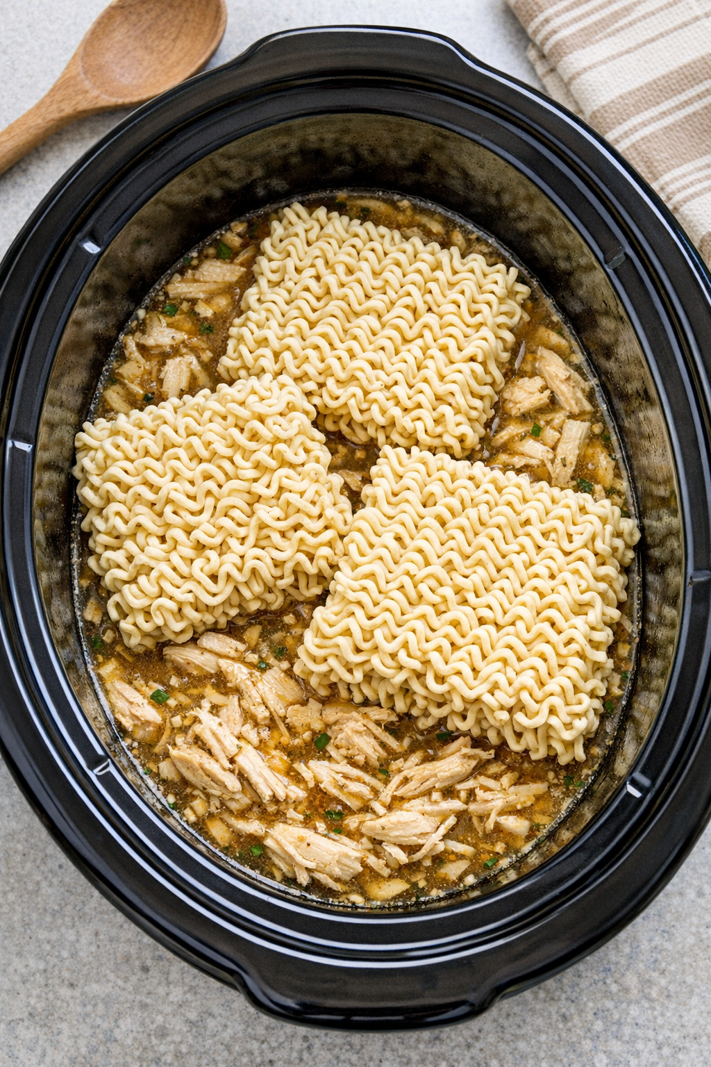 Ramen noodles added to shredded chicken in the slow cooker